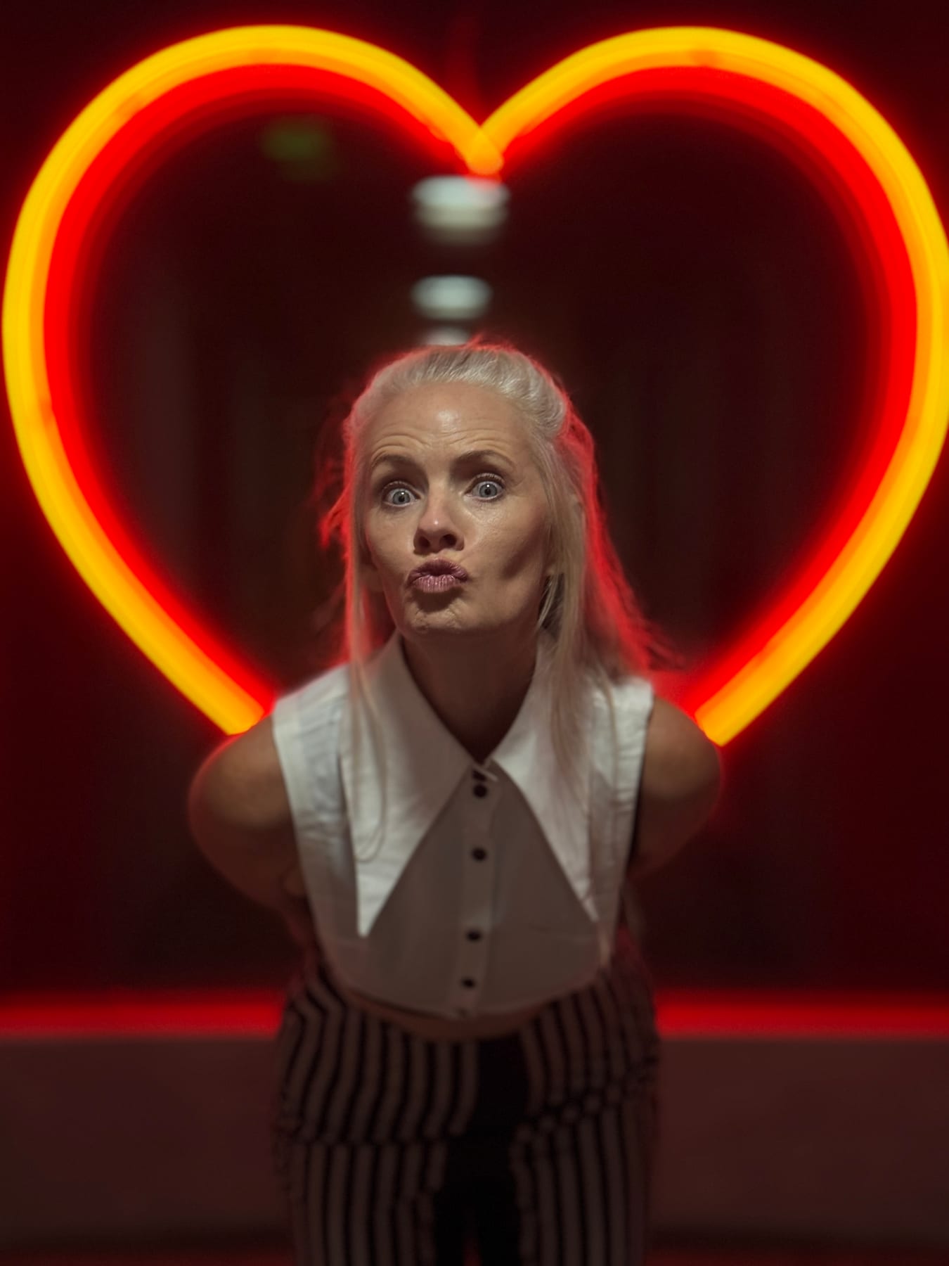 Janelle blowing a kiss beneath a glowing neon heart