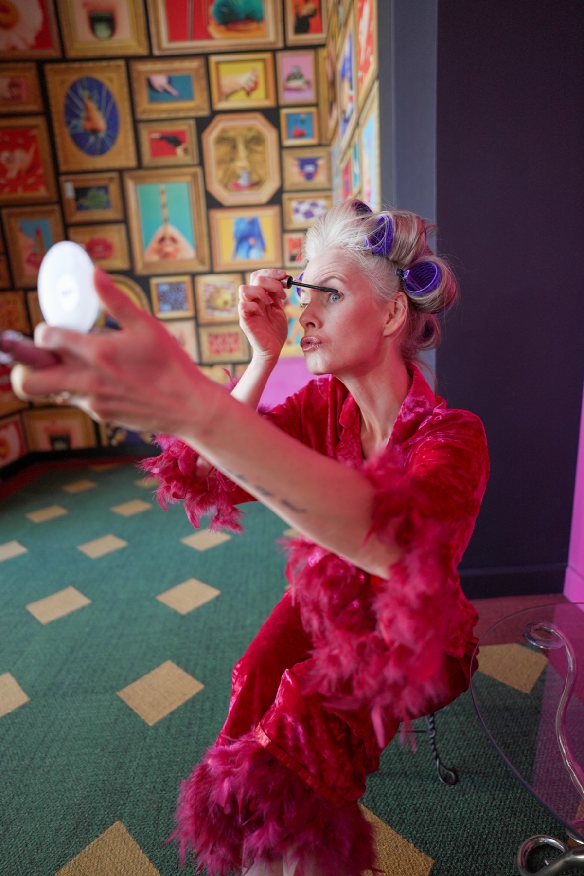 Janelle Nordin playfully applying mascara in a bright pink outfit and hair rollers