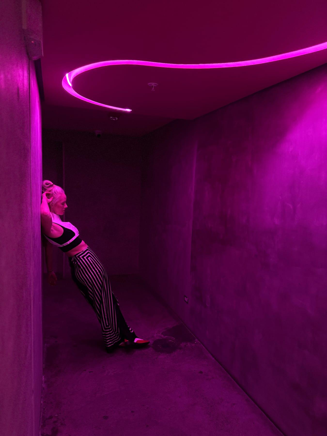 Janelle leaning against a wall beneath a ribbon of purple neon light