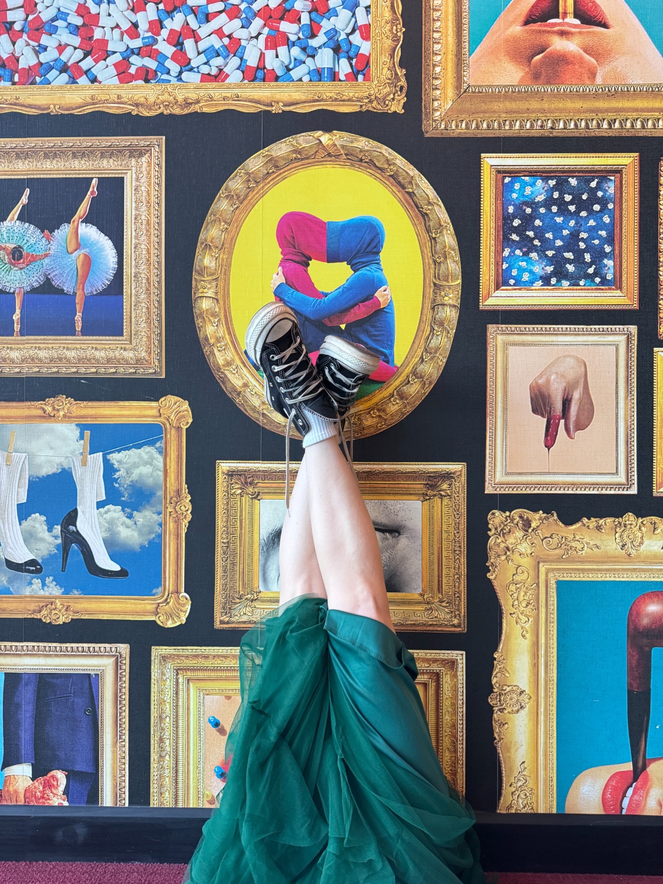 Janelle upside down with her feet against a wall of surreal framed art