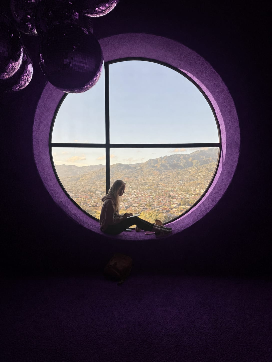Janelle writing on her laptop in a round purple window overlooking a city and mountains